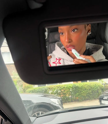Woman applying nourishing lip balm while looking into a car vanity mirror