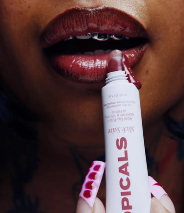 Close-up of person applying Topicals Slick Salve lip balm to glossy, deep red lips with braces.
