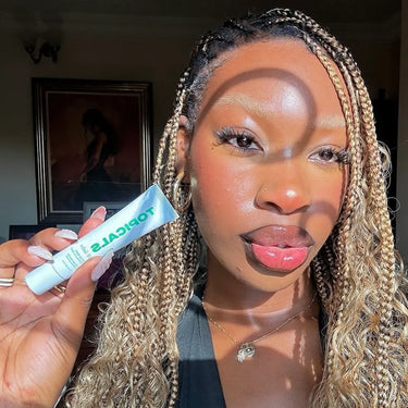Best lip moisturizer showcased by a woman with radiant skin and glossy lips, holding a tube of Topicals skincare in sunlight.