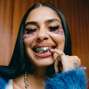 Under eye mask with a branded pattern worn by a woman smiling and showing her silver grills in a stylish indoor setting